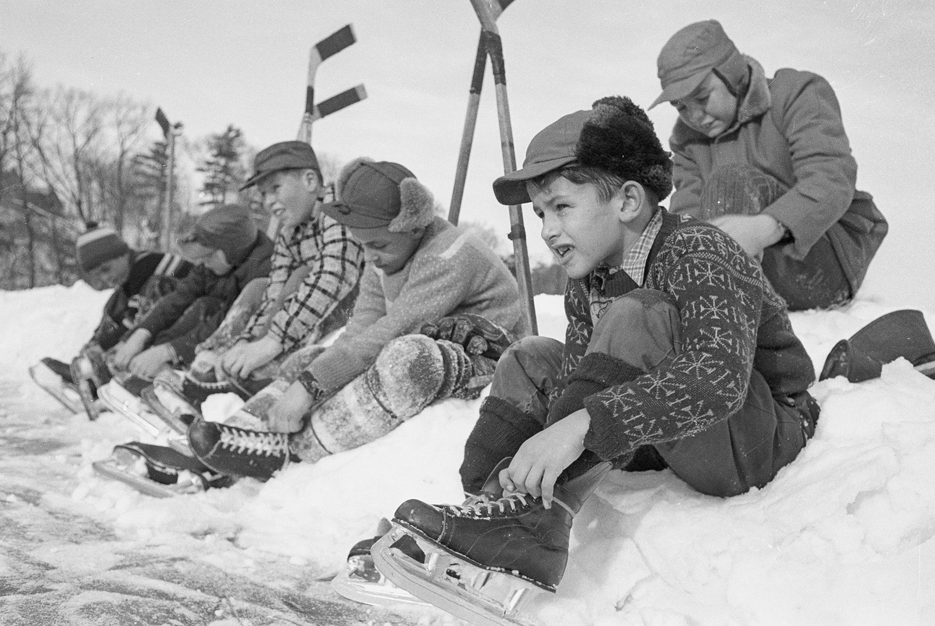 Group of boys sitting on a snowbank, lacing up their hockey skates