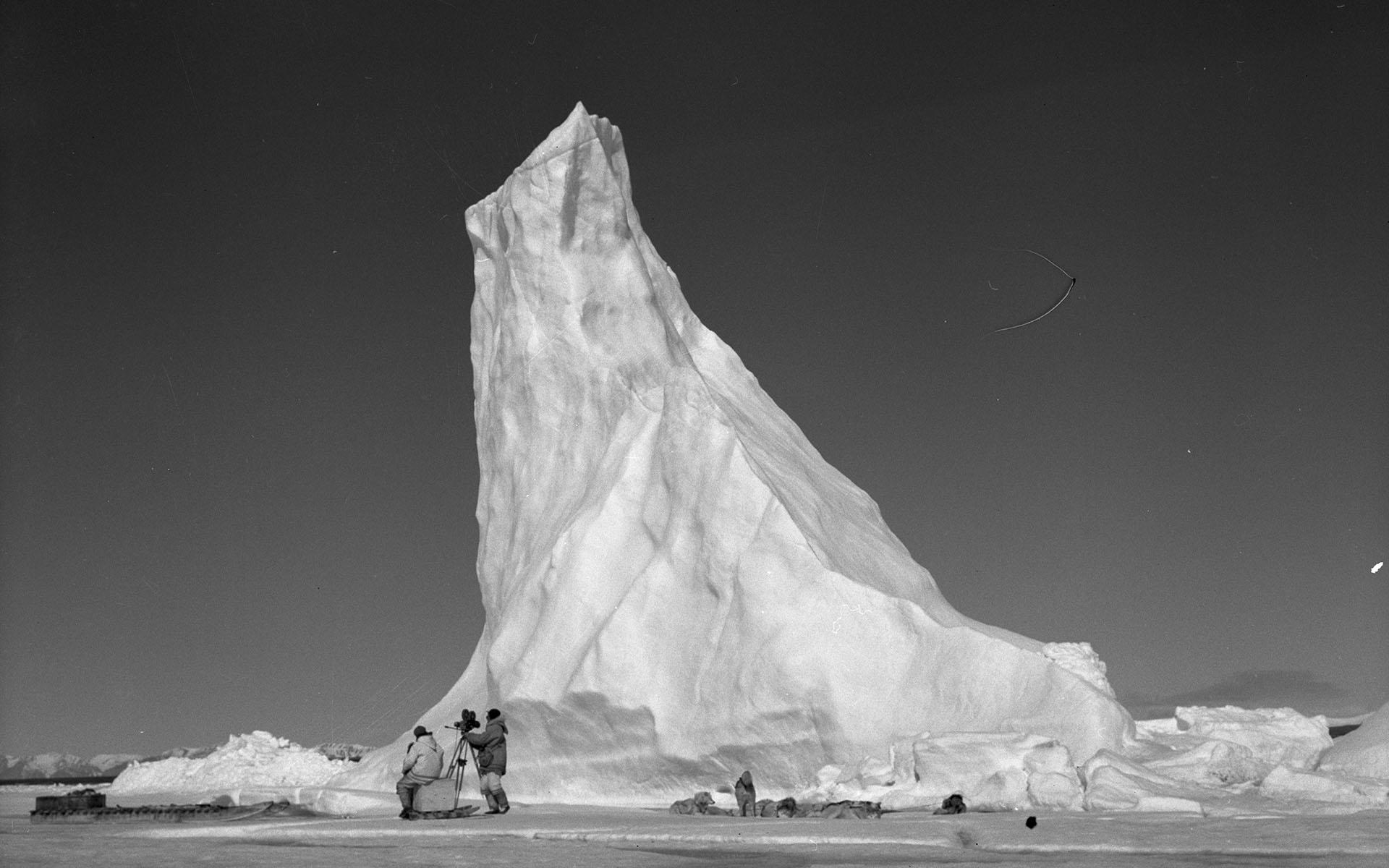 Une équipe de l’Office national du film installe sa caméra près d’un haut iceberg arctique.