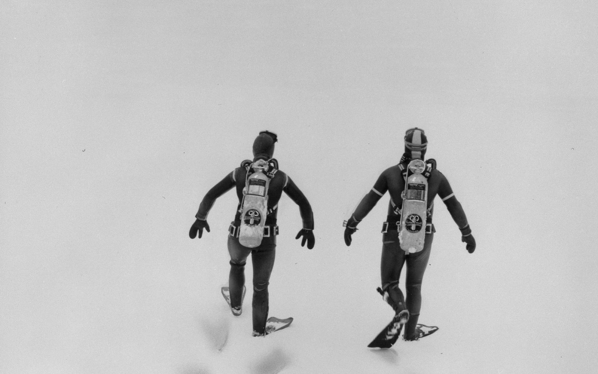 Deux plongeurs vus de dos marchent dans la neige.