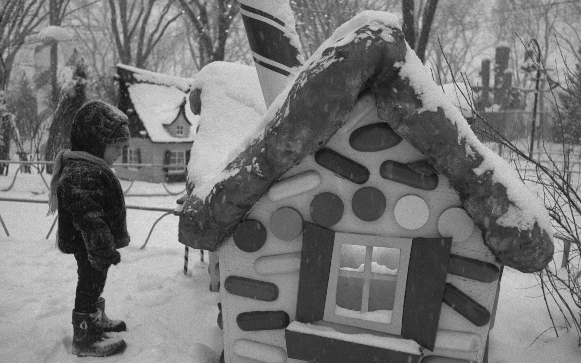 Un jeune enfant en vêtements d’hiver regarde une maisonnette en bonbons.