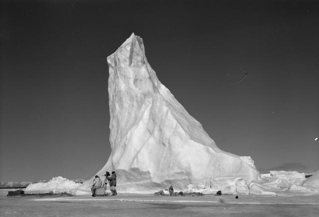 National Film Board crew setting up their camera near a towering arctic iceberg
